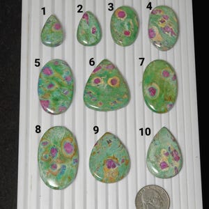 May include: Ten polished gemstones in various shapes, including teardrop and oval. The stones have a green base colour with pink and yellow inclusions. A coin is included for size reference.