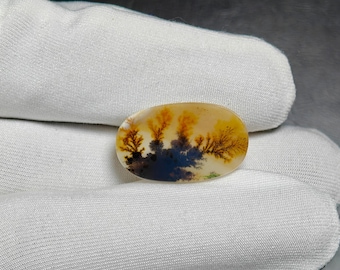 Op de afbeelding: Een ovaalvormige edelsteen met een landschapsontwerp. De steen toont een scène met gele en oranje boomachtige formaties tegen een blauwe en zwarte achtergrond. De steen is ongeveer 3,8 cm lang.