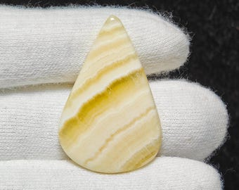 May include: A teardrop-shaped, white and yellow agate cabochon with a banded pattern. The stone is smooth and polished.