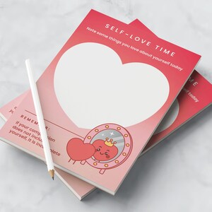 Op de afbeelding: Twee roze "SELF-LOVE TIME" tijdschriften met een wit potlood. Elk tijdschrift heeft een grote hartvorm en de tekst "SELF-LOVE TIME". Eén tijdschrift heeft een cartoonhart met een kroon die in een spiegel kijkt.