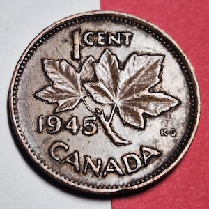 May include: A Canadian one-cent coin from 1945. The coin features two maple leaves, the word "CANADA" at the bottom, and "1 CENT" at the top. The year "1945" is prominently displayed. The coin has a textured, metallic appearance.