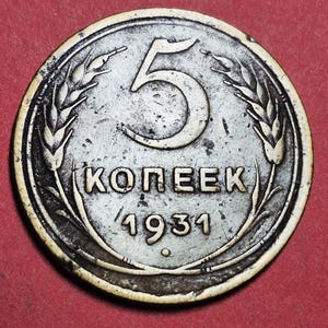 May include: A silver-colored coin with the number 5 prominently displayed. The coin features the text "KOПEEK" and the year "1931". Wheat stalks frame the top and sides of the coin, with a red background.