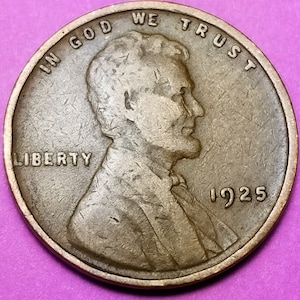 May include: A 1925 Lincoln wheat penny, a copper-colored coin. The obverse features a profile of Abraham Lincoln, the word "LIBERTY", and the phrase "IN GOD WE TRUST". The year "1925" is visible.