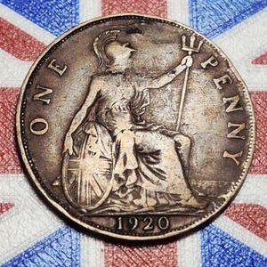 May include: A silver 1920 British penny coin featuring Britannia seated with a shield and trident. The coin is set against a backdrop of the Union Jack flag, with the words "ONE PENNY" and the date "1920" visible.