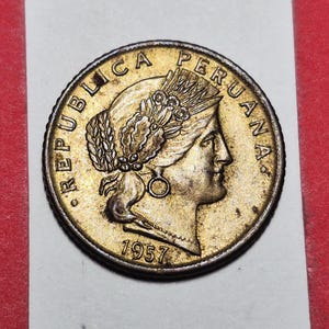 May include: A vintage Peruvian coin from 1957, featuring a profile of a woman with a laurel wreath and the inscription "REPUBLICA PERUANA." The coin has a gold and bronze color with intricate details and a textured edge.