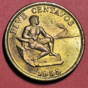 May include: A bronze-colored coin with the text "FIVE CENTAVOS" at the top and the year "1958" at the bottom. The coin features a muscular figure seated near an anvil, holding a hammer. A small island is depicted in the background.