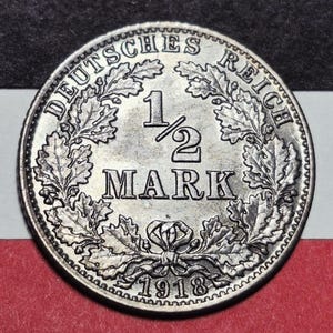 May include: A silver coin from 1918 with the text "DEUTSCHES REICH" around the edge. The coin features the denomination "1/2 MARK" in the center, surrounded by an oak leaf wreath. The year "1918" is at the bottom.