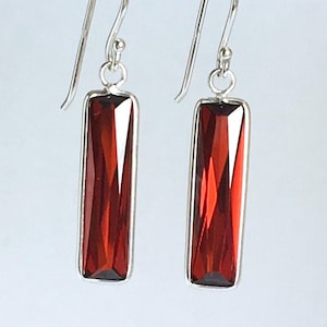 Könnte beinhalten: Ein Paar silberne Ohrhänger mit roten rechteckigen Edelsteinen.