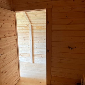 Puede incluir: Una puerta de madera abierta revela una habitaci&oacute;n con suelo y paredes de madera. La habitaci&oacute;n est&aacute; vac&iacute;a, excepto por algunos muebles.