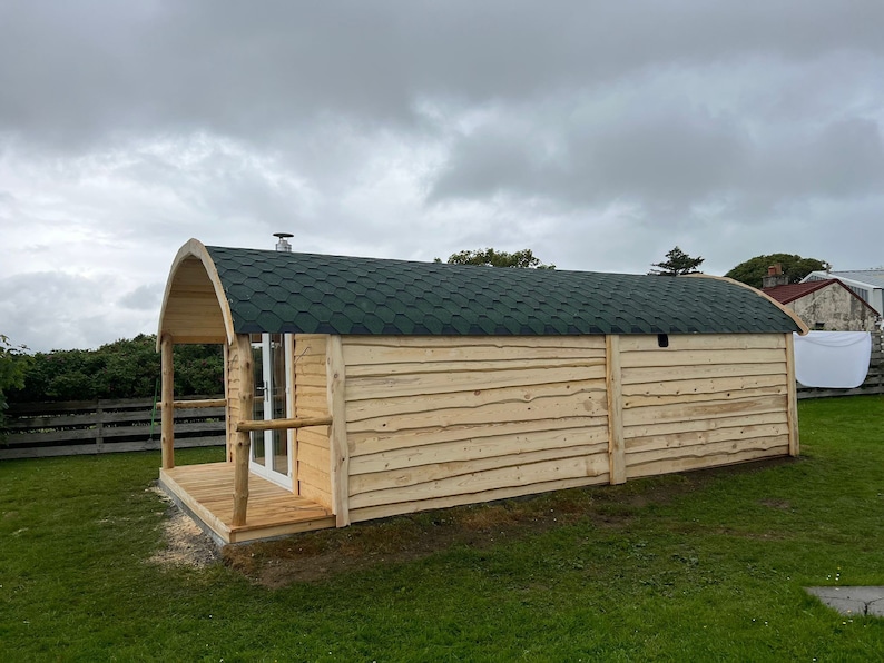 Puede incluir: Una caba&ntilde;a de madera con un techo verde y un peque&ntilde;o porche. La caba&ntilde;a est&aacute; hecha de madera natural y tiene un aspecto r&uacute;stico.