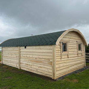 Puede incluir: Una caba&ntilde;a de madera con un techo verde y dos ventanas. La caba&ntilde;a est&aacute; hecha de madera natural y tiene un techo curvo.