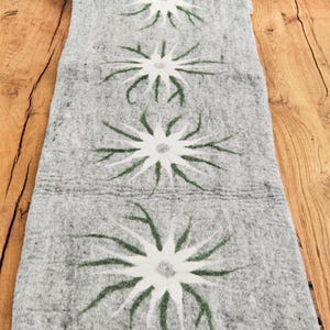 Könnte beinhalten: Ein grauer Tischläufer aus Wolle mit einem sich wiederholenden Muster aus weißen Blüten mit grünen Stielen. Der Läufer ist etwa 35 cm breit und 183 cm lang.