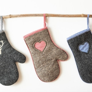 Könnte beinhalten: Drei graue Ofenhandschuhe mit verschiedenen Stickereien. Der erste Handschuh hat ein weißes Reh mit Geweih, der zweite ein rot-weiß kariertes Herz und der dritte ein blau-weiß kariertes Herz.