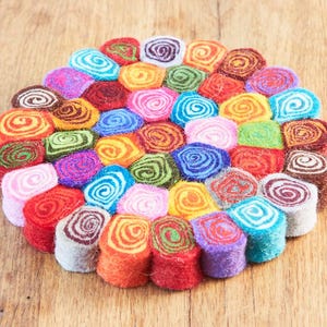 Può includere: Un sottopentola circolare in feltro colorato composto da numerosi piccoli pezzi di feltro arrotolati. I pezzi di feltro sono di vari colori, tra cui rosso, arancione, verde, blu e viola. Il sottopentola è posto su una superficie di legno.