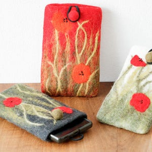 Puede incluir: Tres fundas de teléfono de fieltro con un diseño de amapola. Las fundas son de color rojo, blanco y gris con tallos y hojas verdes. Las fundas tienen un cierre de botón.