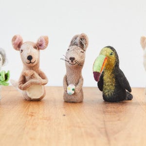 Könnte beinhalten: Fünf Fingerpuppen aus Filz, jede zeigt ein anderes Tier: ein Koala, der ein grünes Blatt hält, ein Känguru, eine Maus, die eine Blume hält, ein Tukan und ein Lama.