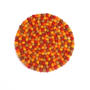 Può includere: Un sottopentola rotondo in feltro con un motivo a mosaico. Il sottopentola presenta un design concentrico con sfumature di rosso, arancione e marrone. È progettato per proteggere le superfici dal calore ed è adatto per l'uso in cucina.