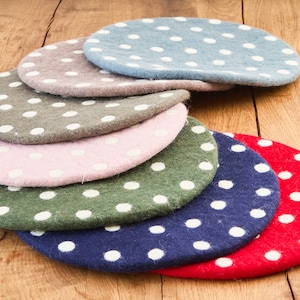 Puede incluir: Conjunto de ocho posavasos redondos de fieltro con lunares blancos en varios colores, incluyendo rojo, azul, verde, rosa y gris. Los posavasos están dispuestos en semicírculo sobre una superficie de madera.