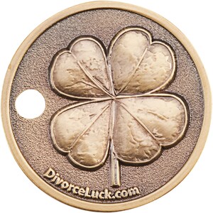 May include: A gold-coloured metal coin with a four-leaf clover design and the text "DivorceLuck.com" on the bottom. The coin has a hole in the top.