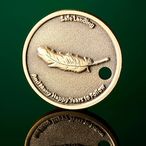 May include: A gold-colored metal token with the words "Safe Landing And Many Happy Years to Follow" and a feather design. The token has a small hole in the center.