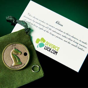 May include: A green velvet pouch containing a silver chess piece charm. The charm depicts a horse and the inscription "Chess Choose Move Wisely". Beside the pouch is a white card with the text "Chess This charm wishes its owner wisdom in their choices, to make decisions by analyzing all the outcomes rather than being reactive. A wish to keep sight of the larger picture, not the small battles. DIVORCE LUCK.COM"