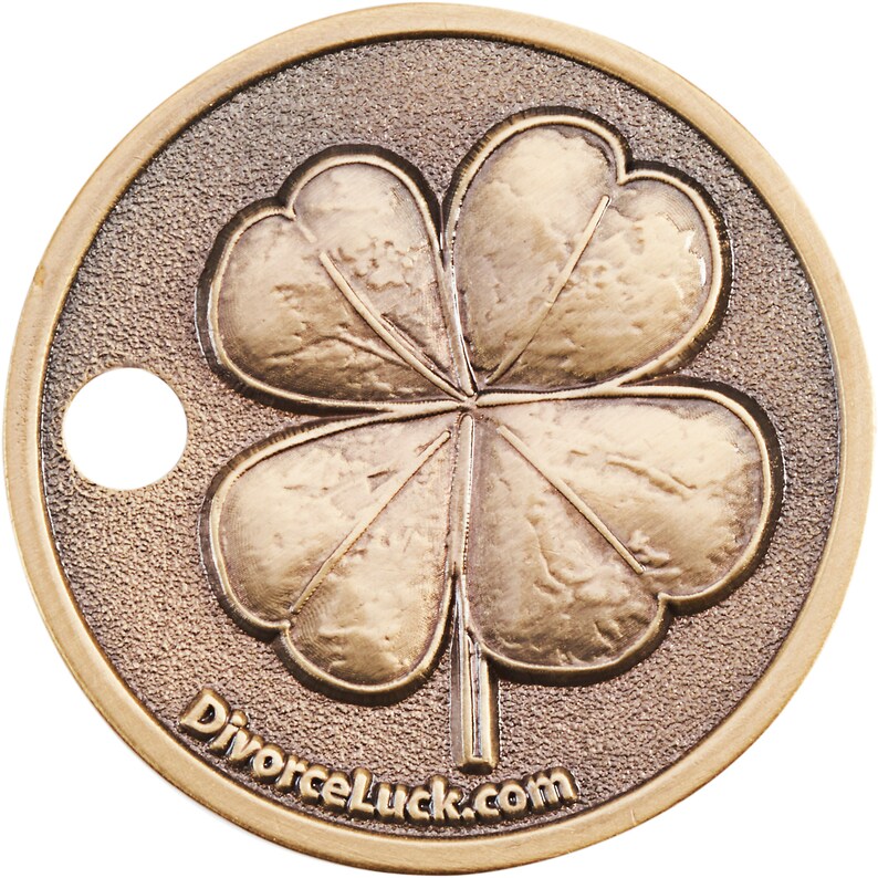 May include: A gold-colored metal coin with a four-leaf clover design and the text "DivorceLuck.com" on the bottom. The coin has a hole in the top.