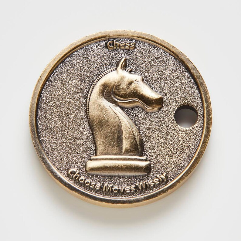 May include: A gold-coloured metal token with a knight chess piece on one side and the words "Chess Choose Moves Wisely" on the other side.