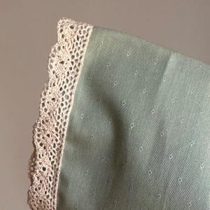 May include: A green fabric with a white lace trim. The fabric has a small, repeating diamond pattern.