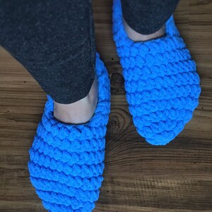 May include: A pair of blue crocheted slippers. The slippers are made of a soft, fluffy yarn and have a simple, rounded shape.