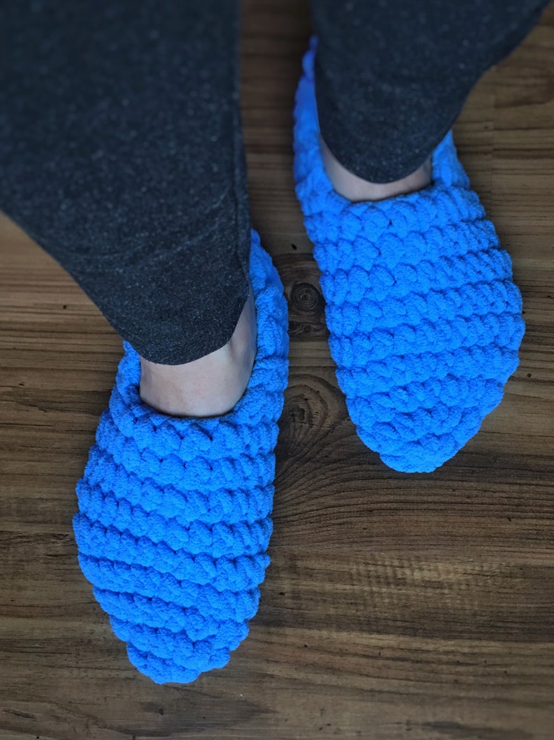 May include: A pair of blue crocheted slippers. The slippers are made of a soft, fluffy yarn and have a simple, rounded shape.