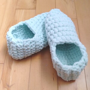May include: A pair of light blue crocheted slippers. The slippers are made with a fluffy yarn and have a simple, comfortable design.