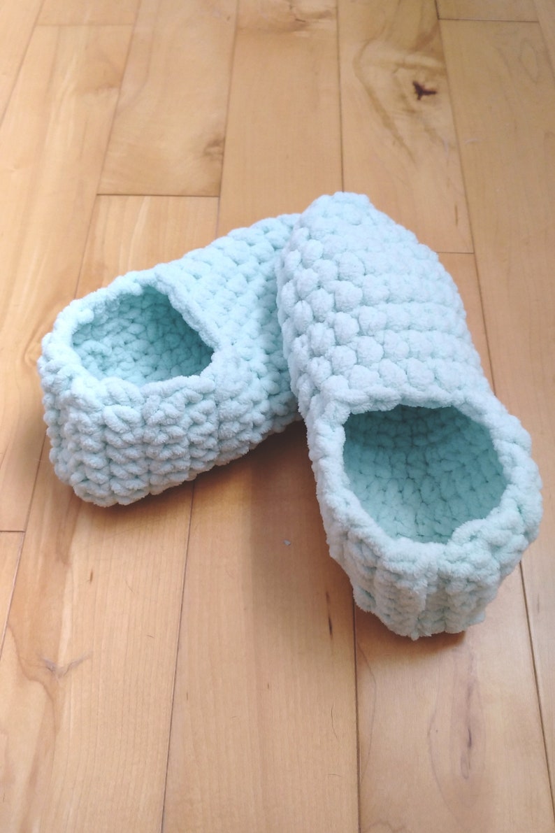 May include: A pair of light blue crocheted slippers. The slippers are made with a fluffy yarn and have a simple, comfortable design.