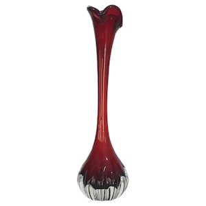 May include: A tall, elegant ruby red glass vase with a flared top and a bulbous, ribbed base. The vase has a long, slender neck and a smooth, glossy finish. The base is clear glass with vertical ridges.
