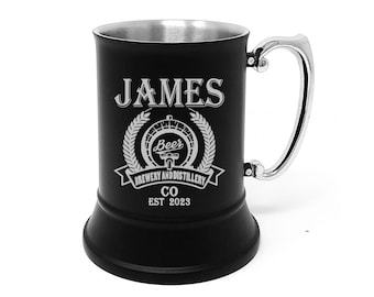 Puede incluir: Un jarro de cerveza de acero inoxidable negro con asa plateada. El jarro está grabado con el texto "JAMES Beer Brewery and Distillery Co EST 2023" y un gráfico de un grifo de cerveza.
