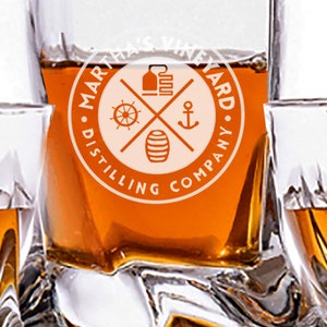 May include: Four clear glass tumblers filled with amber liquid. The tumblers have a logo on the bottom that reads "Martha's Vineyard Distilling Company" with a nautical design.