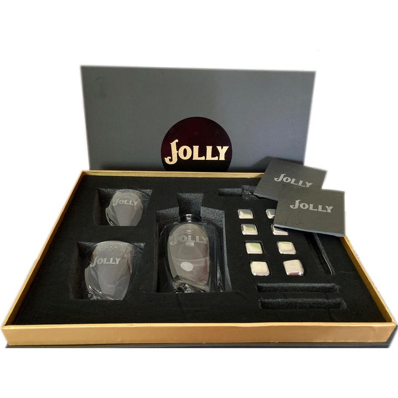 May include: A black gift box with a gold trim, containing a clear glass bottle with the word "JOLLY" etched on it, two clear glasses with the same etching, and a set of silver ice cubes. The box also includes two black coasters with the word "JOLLY" printed on them.
