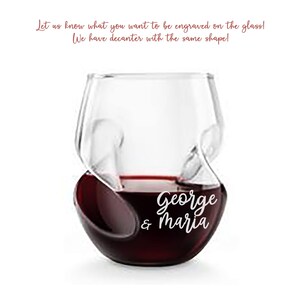 Könnte beinhalten: Ein klares, stieloses Weinglas, gefüllt mit Rotwein, mit einem einzigartigen geschwungenen Design. Das Glas ist mit den Namen "George & Maria" graviert. Der Text oben lautet: "Teilen Sie uns mit, was Sie auf dem Glas graviert haben möchten! Wir haben eine Karaffe mit der gleichen Form!"
