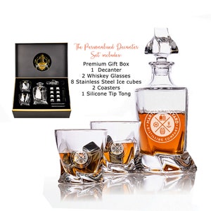 May include: A personalized decanter set with a clear glass decanter, two whiskey glasses, and eight stainless steel ice cubes. The decanter and glasses feature a logo that says "Maritime Distillery Company". The set also includes two coasters and a silicone tip tong. The set comes in a black gift box.