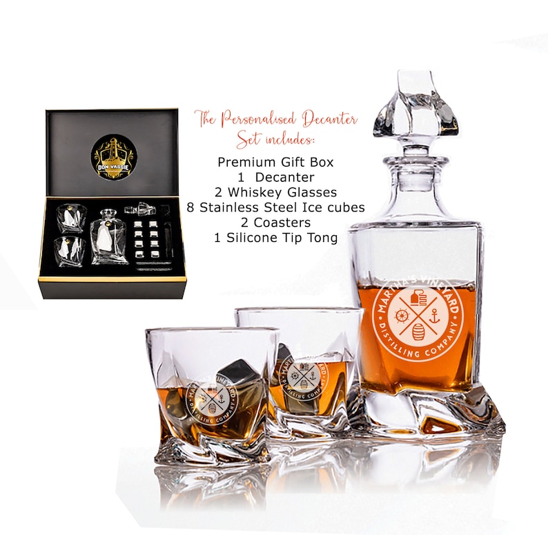 May include: A personalized decanter set with a clear glass decanter, two whiskey glasses, and eight stainless steel ice cubes. The decanter and glasses feature a logo that says "Maritime Distillery Company". The set also includes two coasters and a silicone tip tong. The set comes in a black gift box.