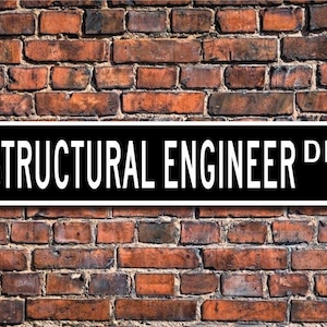 May include: A black and white street sign that reads "STRUCTURAL ENGINEER DR" is mounted on a weathered brick wall. The sign has a rectangular shape with rounded corners and is centered in the image. The brick wall is made of red and brown bricks.