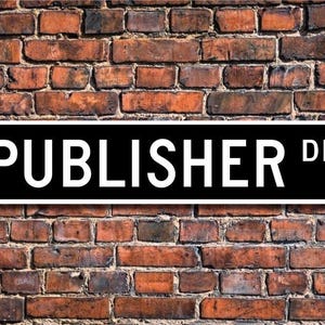 May include: Black and white street sign with the text "PUBLISHER DR." on a brick wall background.