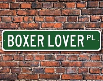 May include: Green street sign with white lettering that reads "BOXER LOVER PL."