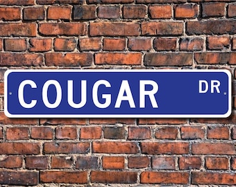 Może przedstawiać: Niebieski i biały znak drogowy z napisem "COUGAR DR."
