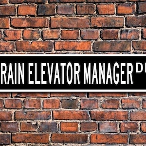 May include: Black and white sign with the text "Grain Elevator Manager Dr." on a brick wall.