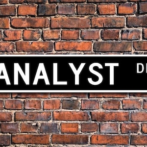 May include: Black and white street sign with the text "ANALYST DR." in white letters on a black background.