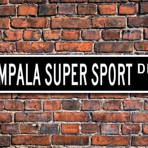 以下が含まれることがあります： 白黒の街路標識で、白い文字で「IMPALA SUPER SPORT DR.」と書かれています