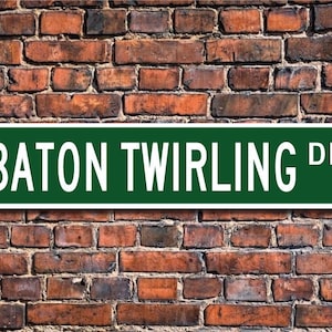 May include: A green street sign with white lettering that reads "BATON TWIRLING DR."