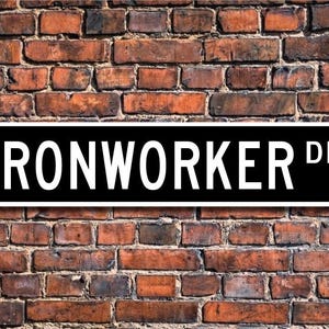 Puede incluir: Un letrero de calle blanco y negro con el texto "IRONWORKER DR." en letras blancas.