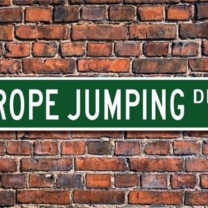 Può includere: Cartello stradale verde con scritta bianca "ROPE JUMPING DR."