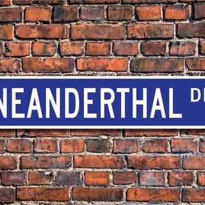Peut inclure: Un panneau de rue bleu avec des lettres blanches qui indiquent "NEANDERTHAL DR."